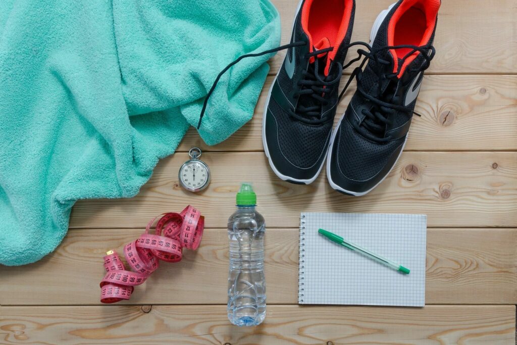 Personal training photo with water bottle, turquoise towel, notebook, stopwatch, and black sneakers.