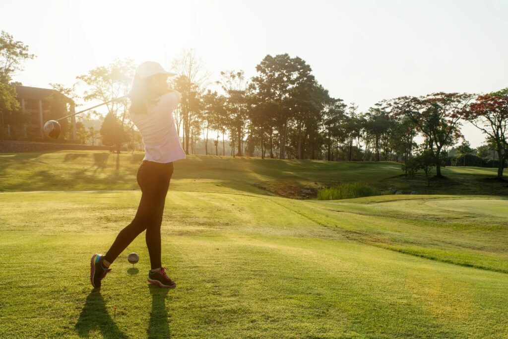 Woman in pink shirt and black leggings taking a swing at the golf ball on the course.