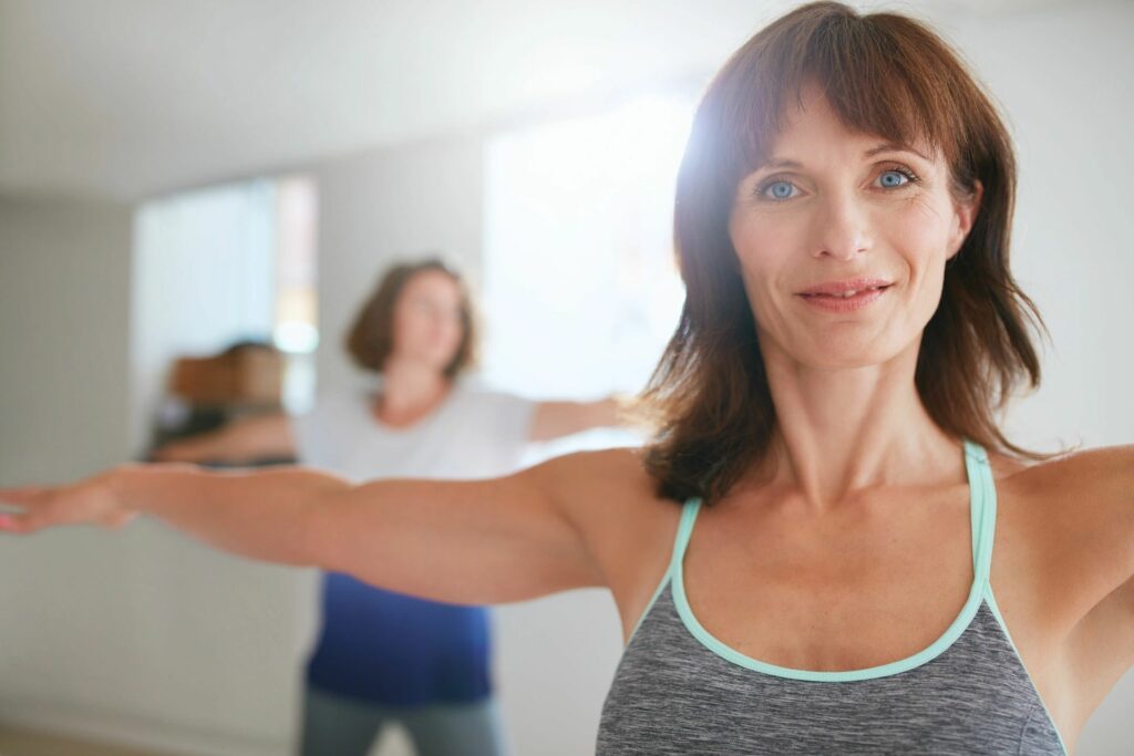 Blue-eyed woman with gray and turquoise tank top on training in a fitness class.