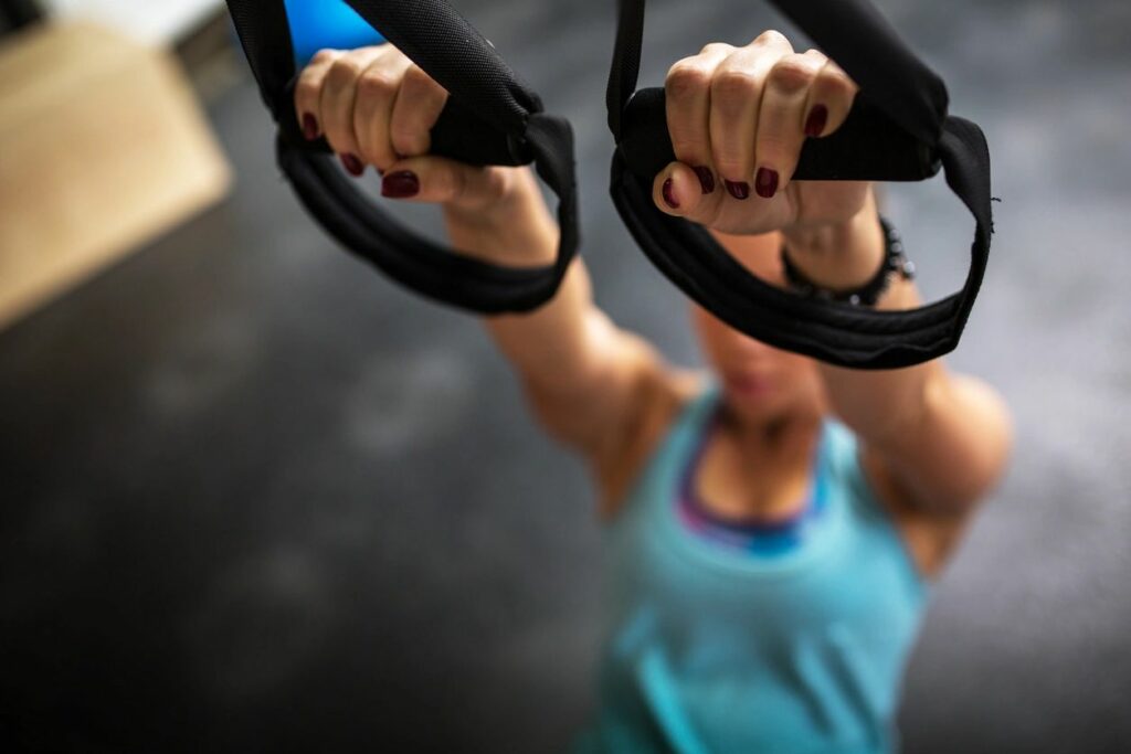 Woman with turquoise tank top and burgundy nails training at the gym.