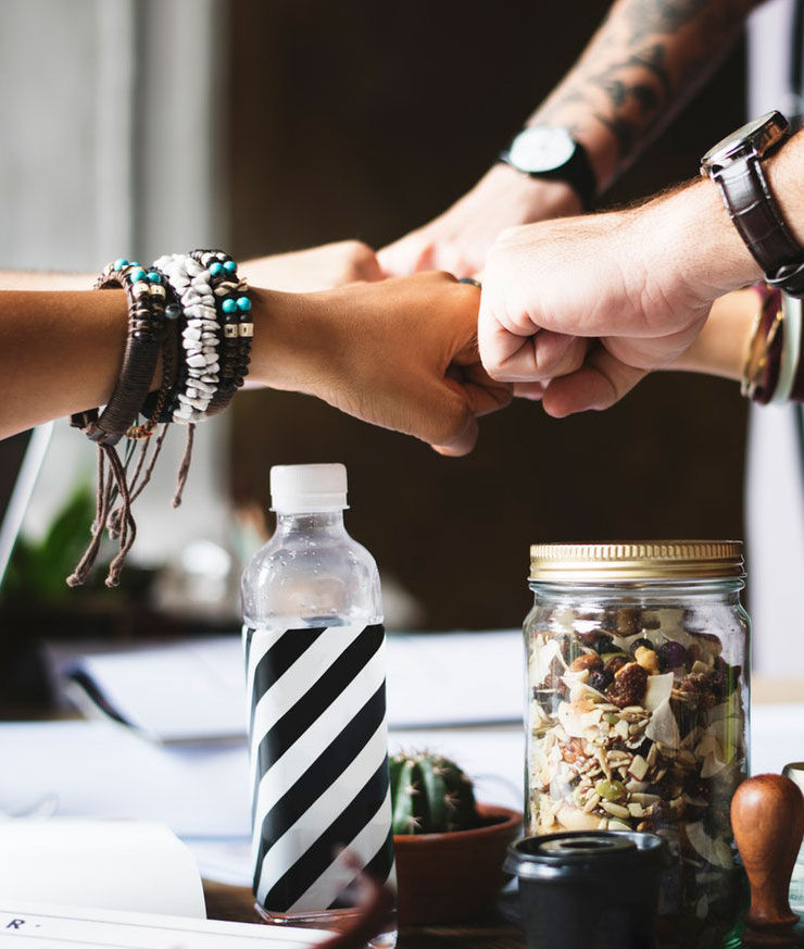 Employees putting their hands in over a table with a water bottle and granola snacks in the foreground.