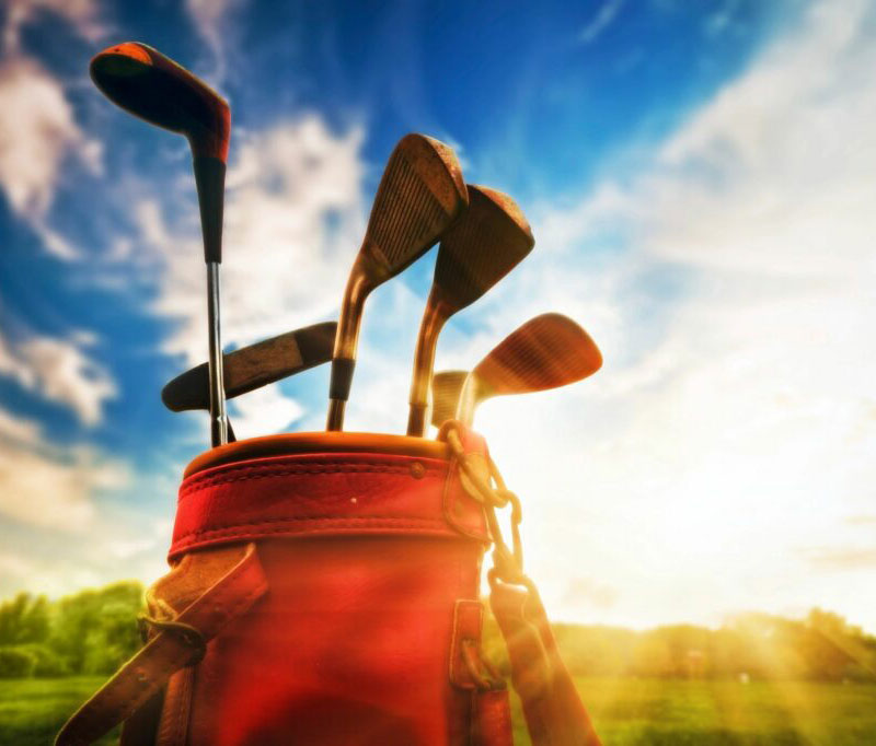 Red golf bag with golf clubs with blue skies and greens in the background