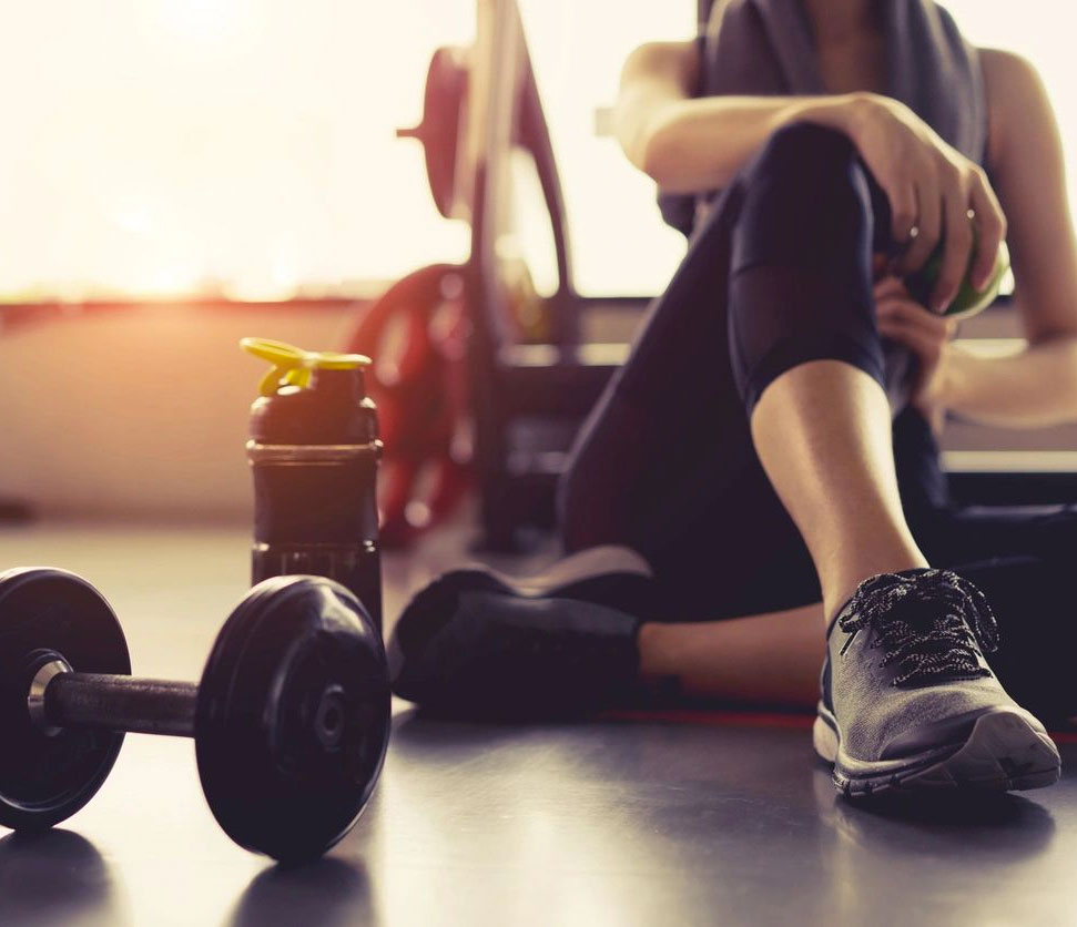 Girl in gym sitting down on the floor with a water bottle and dumbbell nearby.