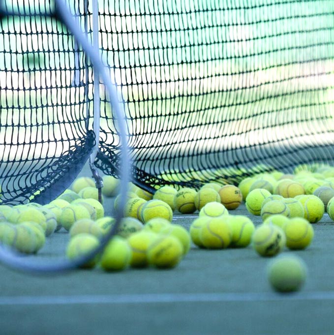 a bunch of tennis balls on the court with a racquet in the foreground
